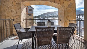 Une terrasse extérieure en pierre, avec des arches, meublée de mobilier en osier et offrant une vue sur une montagne enneigée et des bâtiments.