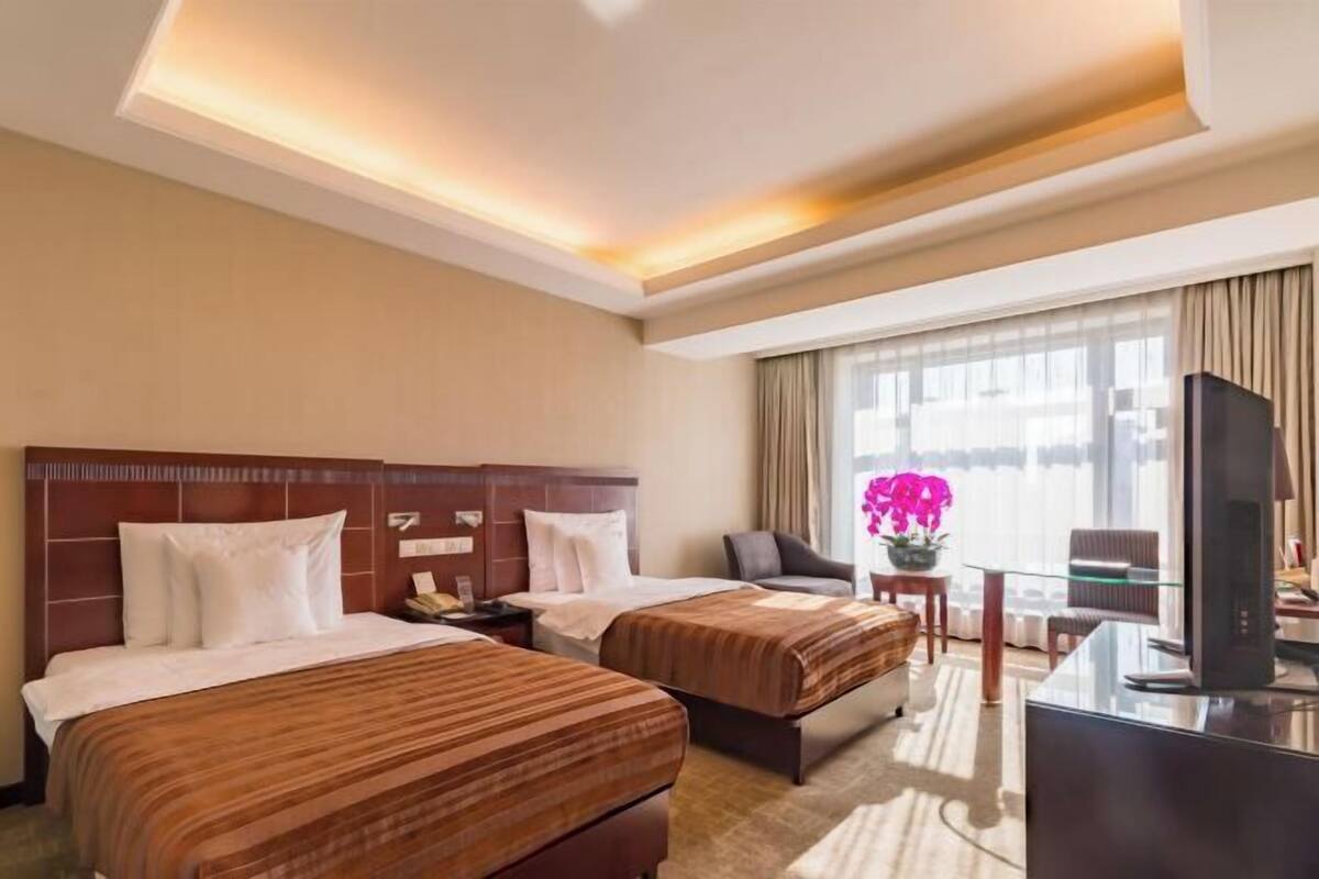 A hotel room with two beds, a desk, a television, and a window with curtains.