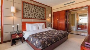 A hotel room with a large bed, a nightstand, a wall-mounted lamp, and a wooden wardrobe.