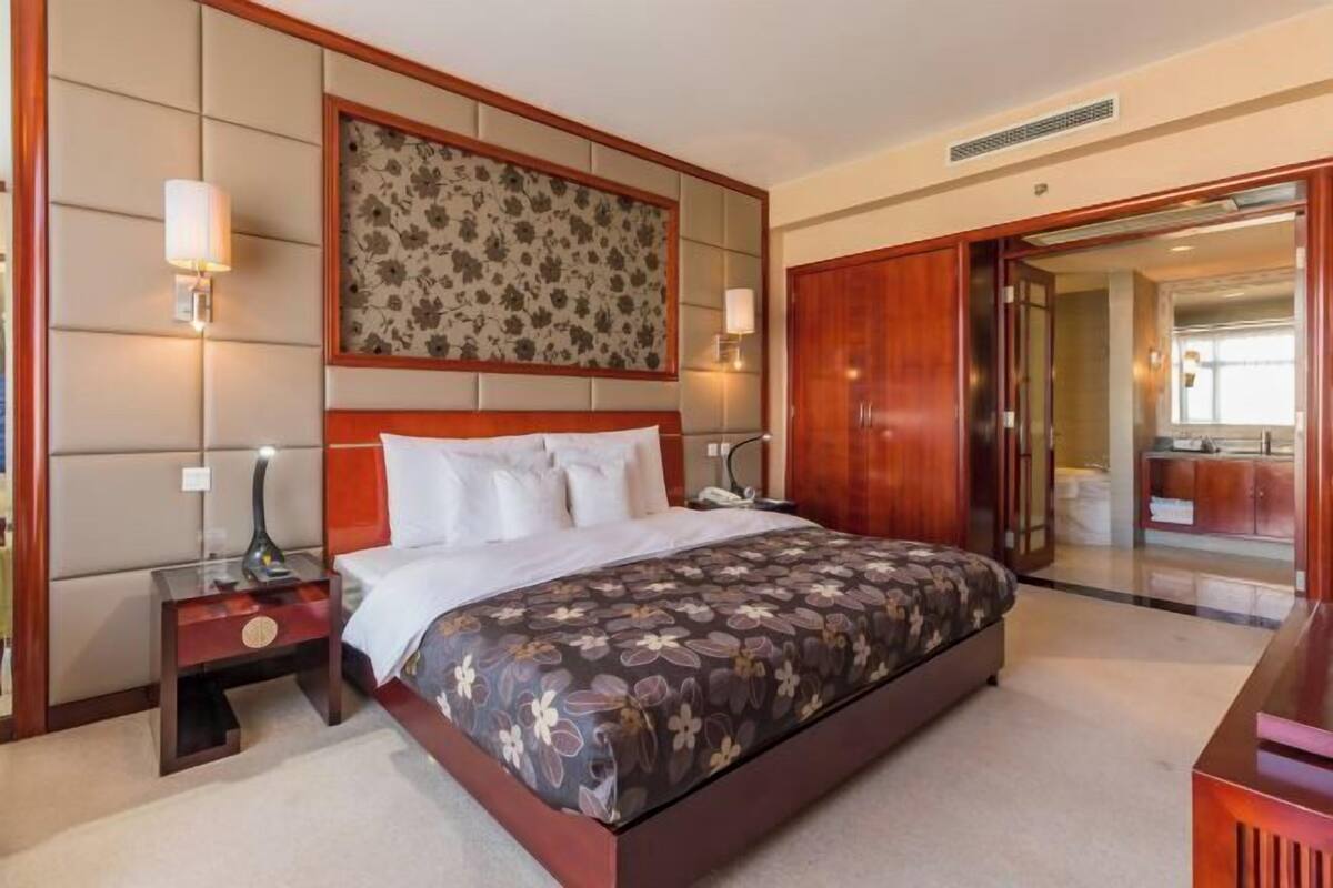 A hotel room with a large bed, a nightstand, a wall-mounted lamp, and a wooden wardrobe.