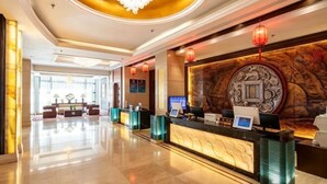 A hotel reception area with a modern design, featuring a reception desk, a chandelier, and a large wall mural.