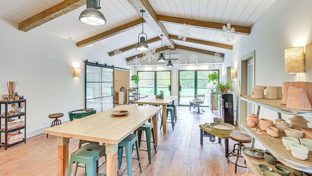 Una cocina amplia con vigas de madera, una mesa larga, taburetes y estantes con cerámica.