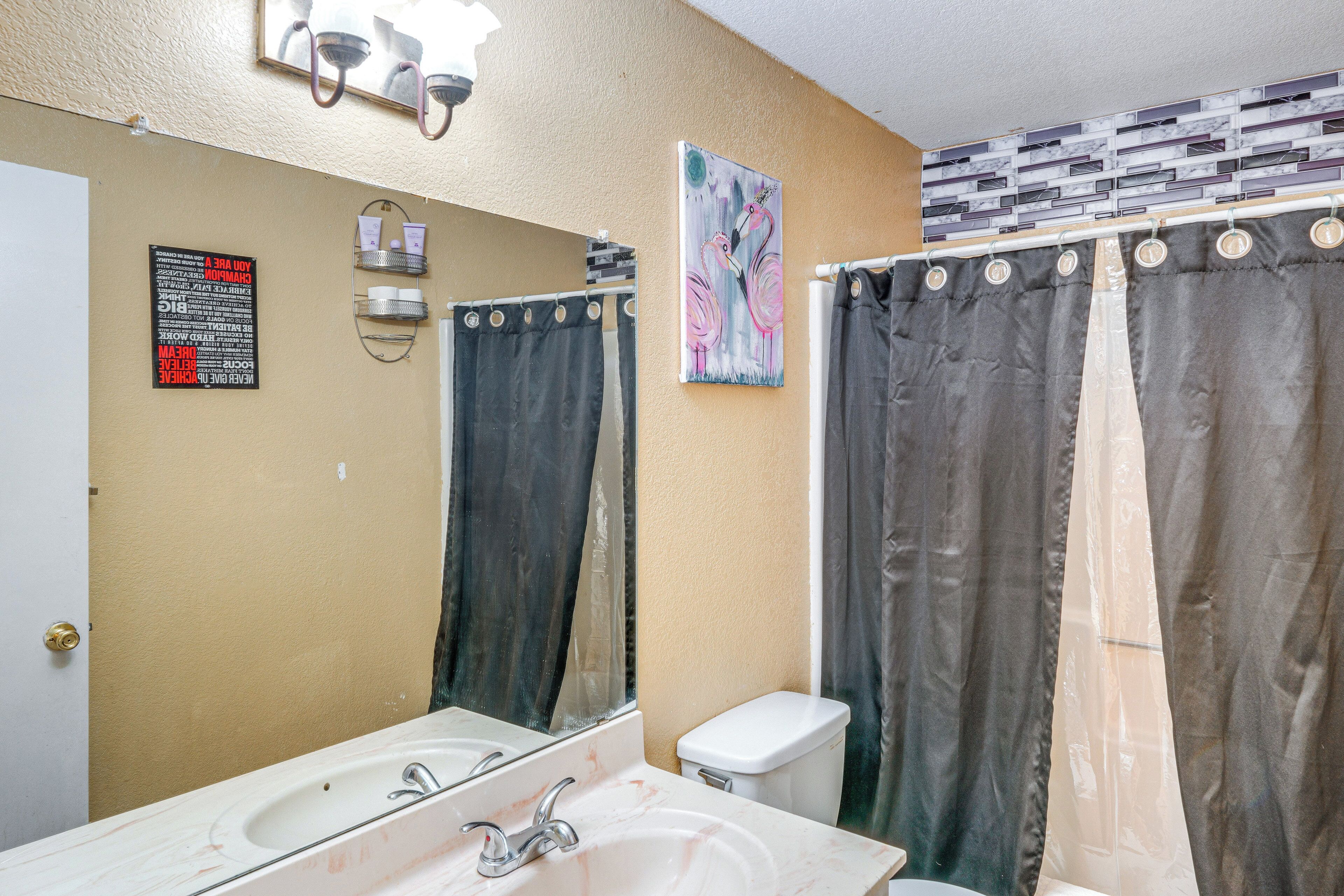 Une salle de bain équipée d’un lavabo, d’un miroir, de toilettes et de deux rideaux de douche.