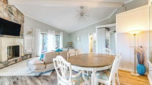 Un coin repas avec une table ronde et des chaises blanches, une cheminée en pierre et un lustre.