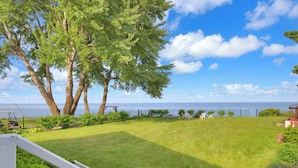 Une cour arrière verdoyante avec vue sur la mer, une terrasse en bois et une clôture blanche.