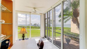 A room with a large window, a ceiling fan, a table, and a chair. - Walk to Stuart Beach: Resort Condo w/ Water View! (Stuart)