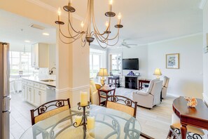 A modern kitchen with white cabinets, a dining area with a glass table, and a living room with a TV and seating.