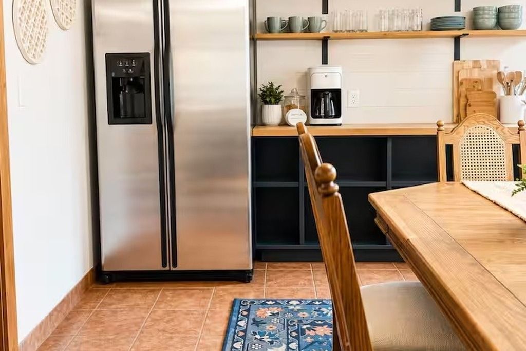 A kitchen with a stainless steel refrigerator, a coffee maker, and a wooden dining table with a chair.