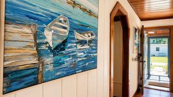 Un pasillo con un cuadro grande de barcos en el agua, paneles de madera y una puerta que da a un espacio exterior luminoso.