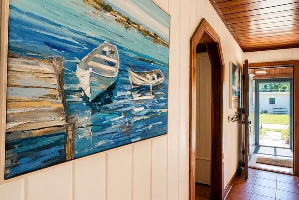 A hallway with a large painting of boats on water, wooden paneling, and a door leading to a bright outdoor area.