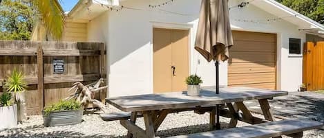 A wooden picnic table with benches, a potted plant, and a string of lights in a backyard.