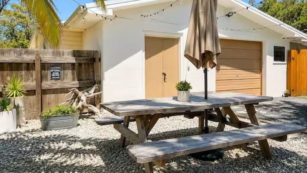 A wooden picnic table with benches, a potted plant, and a string of lights in a backyard.