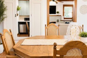 Un comedor con mesa y sillas de madera, una cocina al fondo y un ventilador de techo.