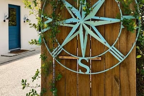 A wooden gate with a compass sign, a blue door, and a small porch area.