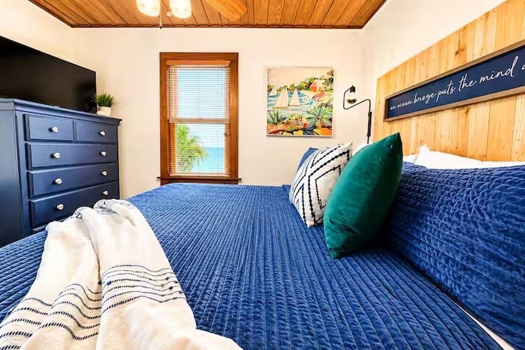 A bedroom with a bed, a dresser, a window, and a wall-mounted artwork.