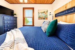 A bedroom with a bed, a dresser, a window, and a wall-mounted artwork.