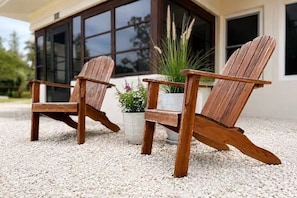 Deux fauteuils Adirondack en bois, placés sur une surface de gravier, avec des plantes en pot à proximité.