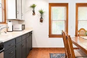 Una cocina con microondas, armarios, un lavamanos y dos plantas en macetas.