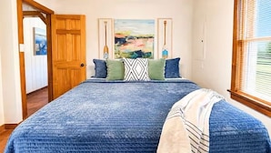 A bedroom with a large bed, wooden ceiling, and a painting on the wall.