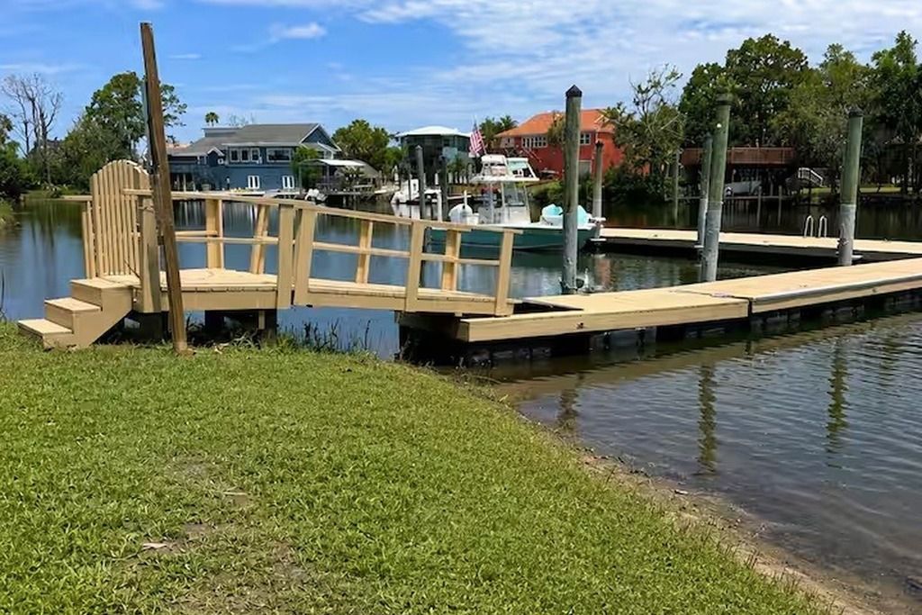 Une jetée en bois s’étendant dans une étendue d’eau calme, avec une rive herbeuse d’un côté.