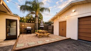A backyard with a picnic table, a grill, and a palm tree.