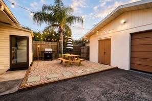 Un patio trasero con una mesa de picnic, una parrilla y una palmera.