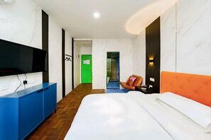 Ein modernes Hotelzimmer mit einem Flachbildfernseher, einem blauen Schrank, einem Bett mit weißer Bettwäsche und einer grünen Tür im Hintergrund.