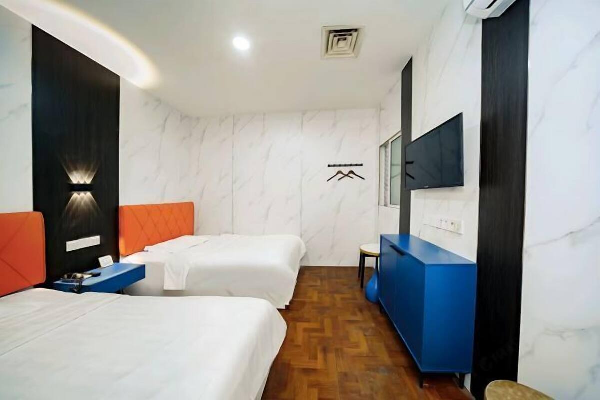 A hotel room with two beds, a blue dresser, a TV mounted on the wall, and a wooden floor.