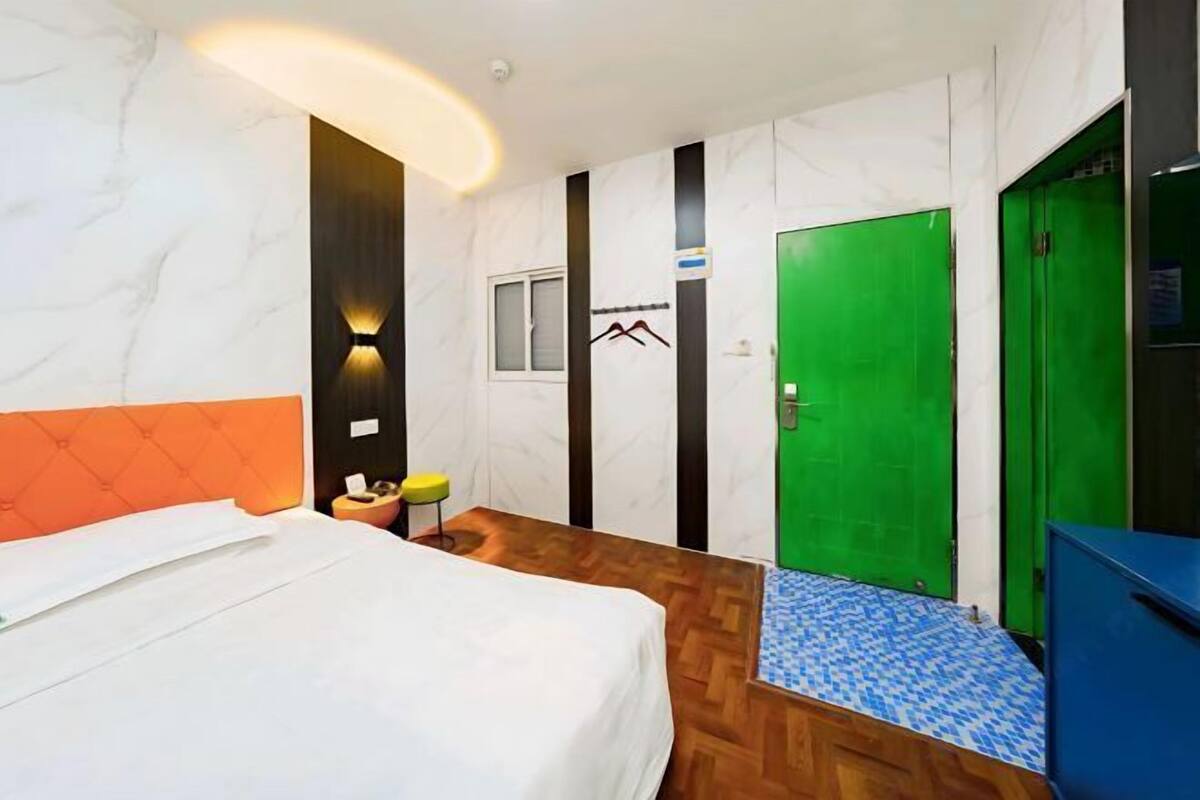 A hotel room with a bed, a small table with a chair, a green door, and a blue cabinet.