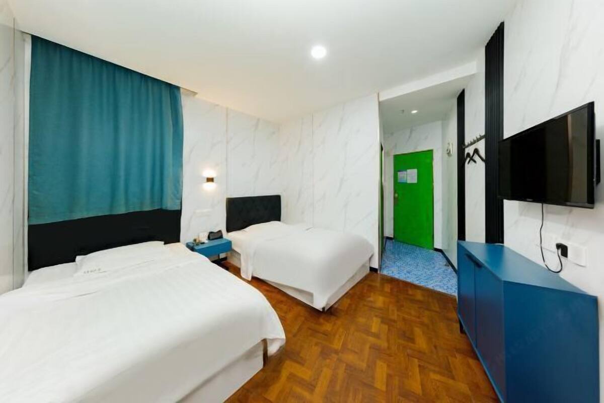 A hotel room with two beds, a blue dresser, a television, and a green door in the background.