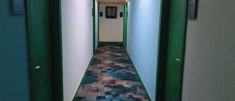 Un pasillo estrecho con puertas verdes a cada lado y una alfombra estampada.