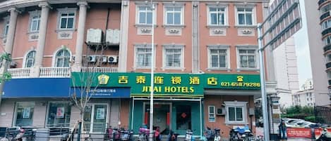 A hotel with a green signboard, multiple windows, and a balcony.