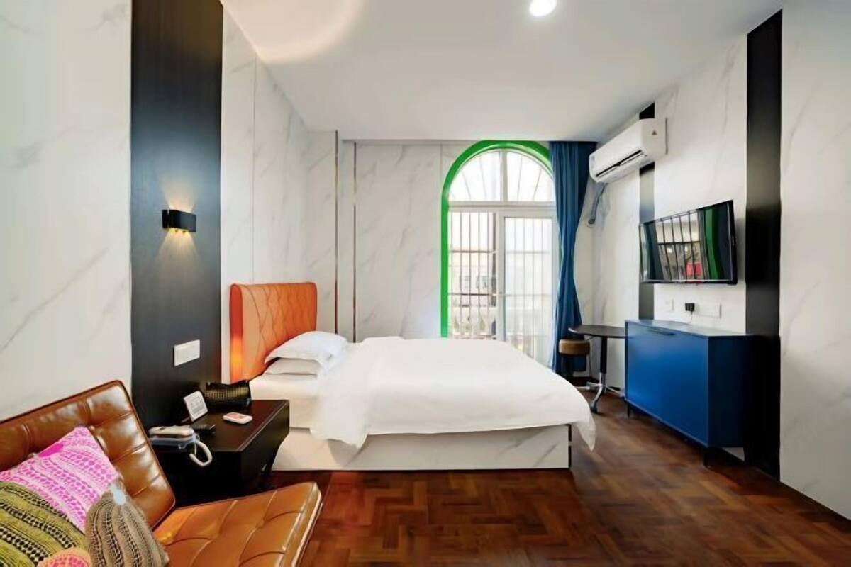 A hotel room with a bed, a desk, a chair, a TV, and an air conditioning unit.