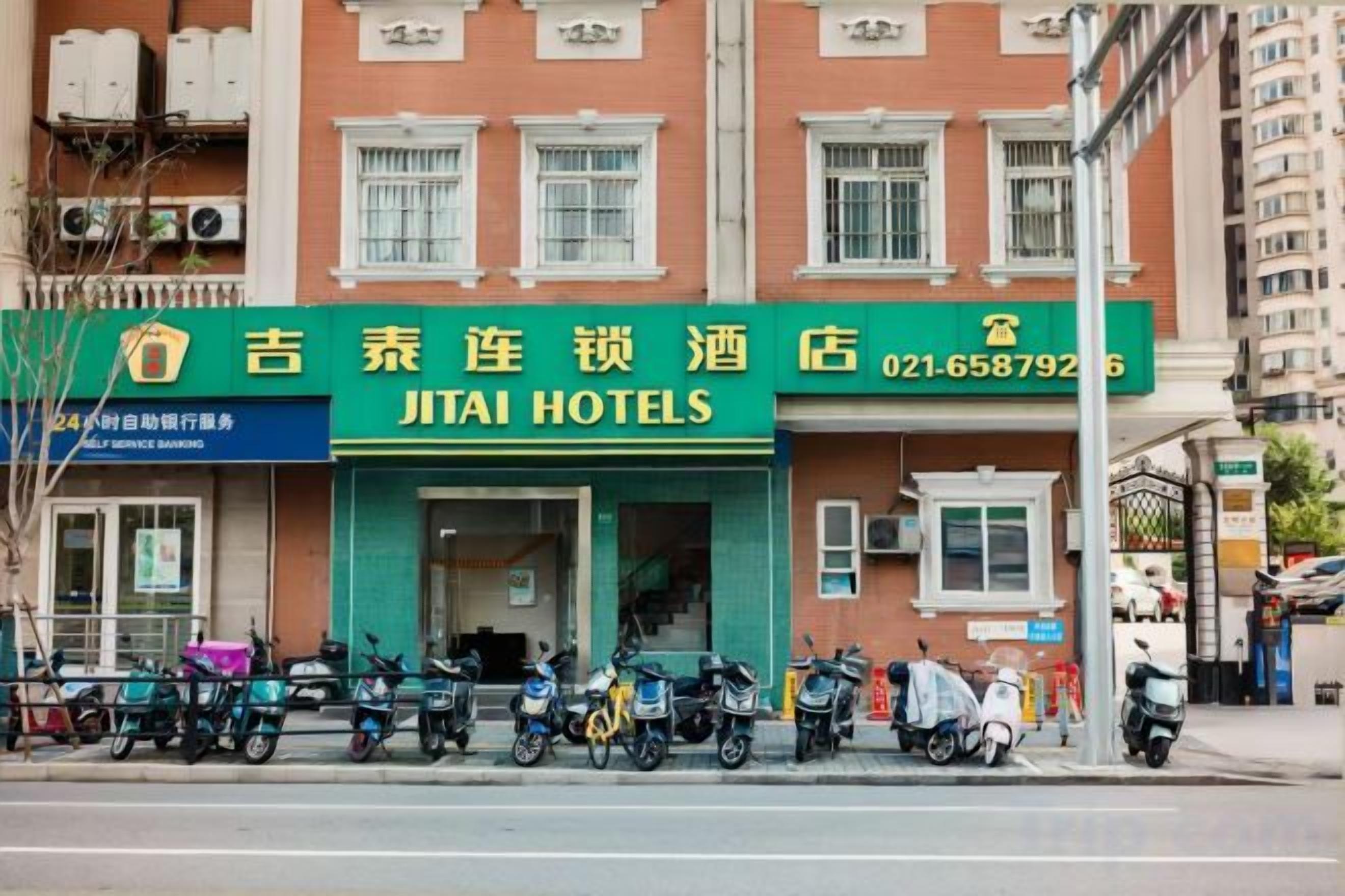 A hotel with a green signboard, multiple motorcycles parked in front, and a clear view of the entrance.