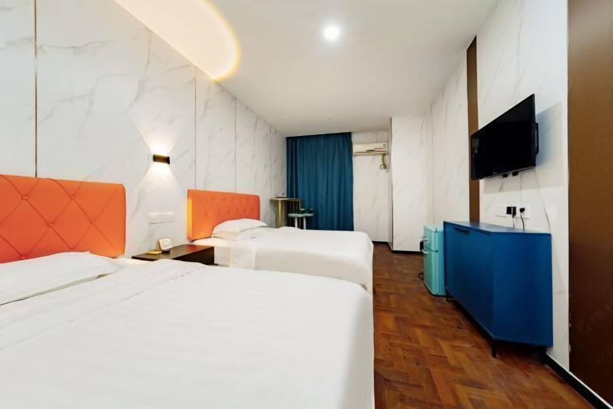 A hotel room with two beds, a blue minibar, a TV, and a bathroom with a blue curtain.