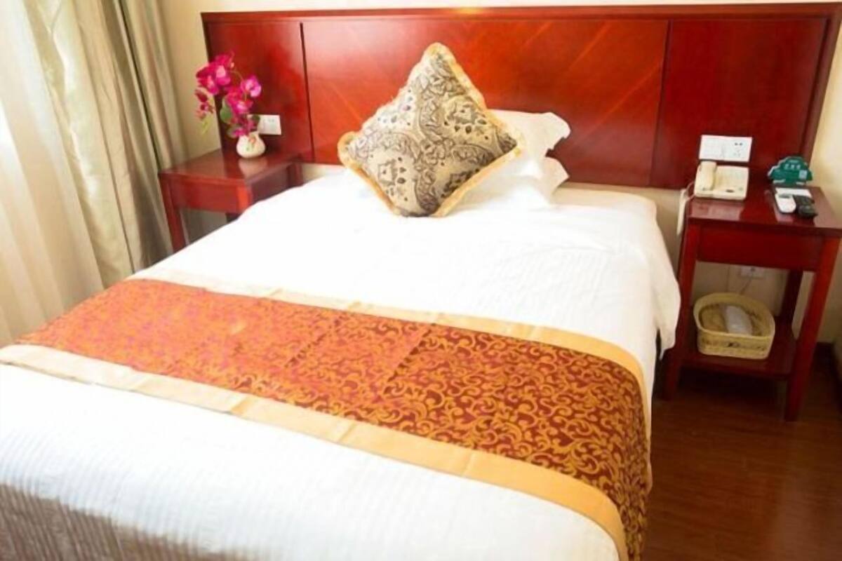 A hotel room with a bed, a nightstand with a phone, and a decorative pillow.