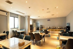 Un comedor de hotel con mesas y sillas, una cocina al fondo y un ventanal grande a la izquierda.