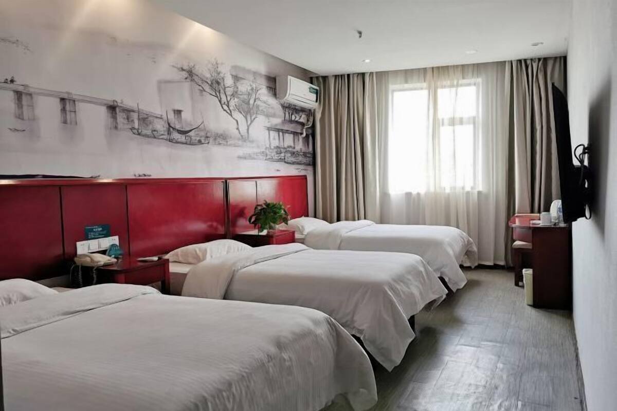 A hotel room with three beds, a red headboard, a large wall mural, and a window with curtains.