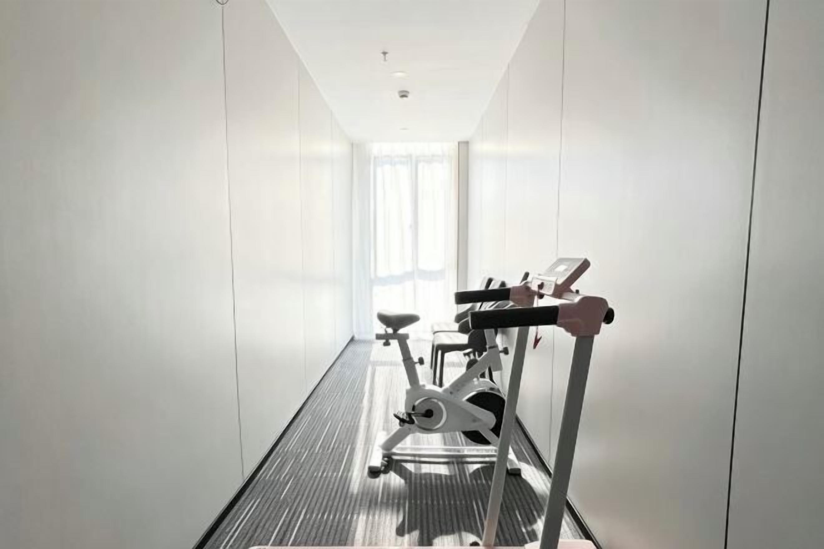 A hotel corridor with a treadmill, a stationary bike, and a mirror.
