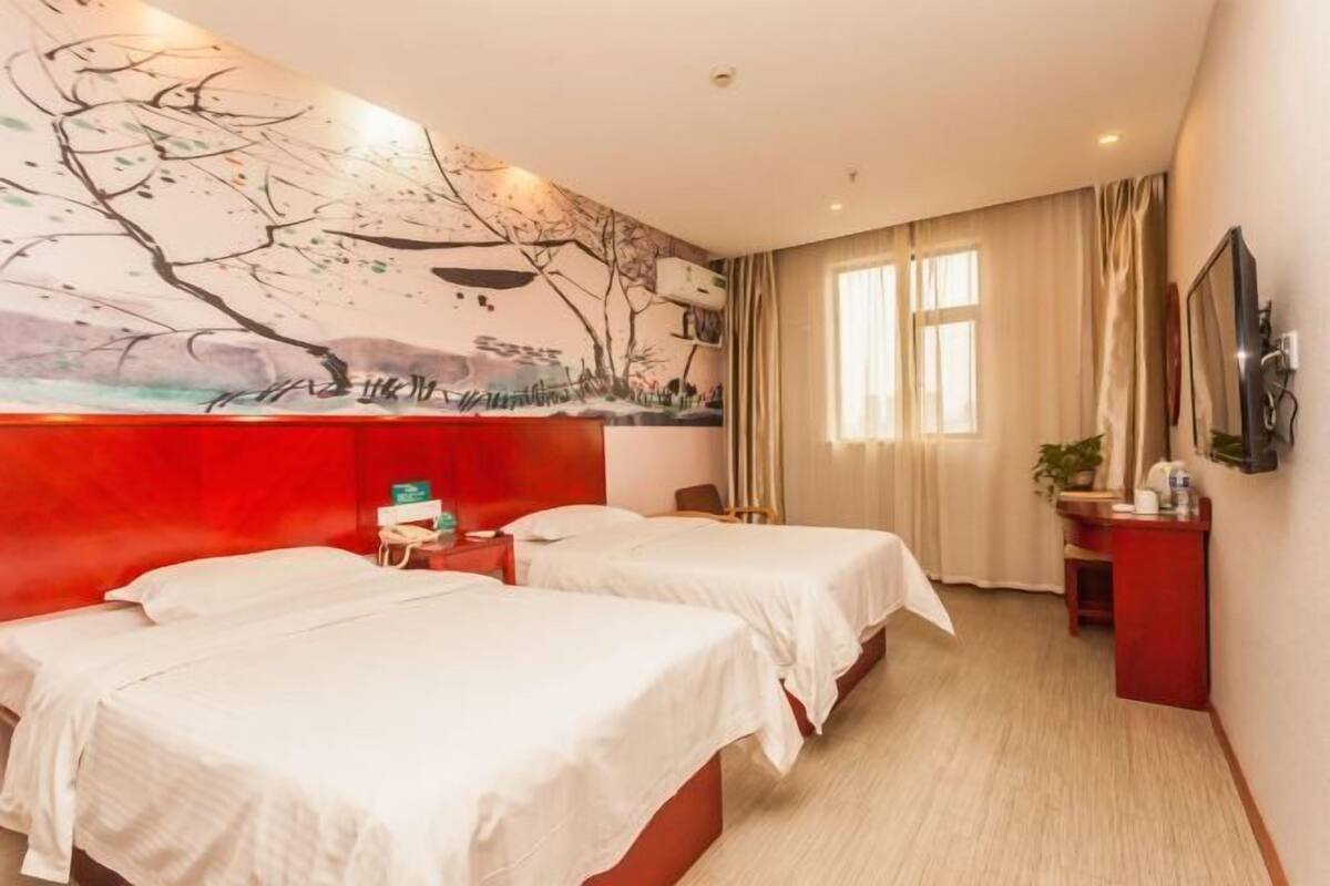 A hotel room with two beds, a red accent wall, a painting, a TV, and a window with curtains.