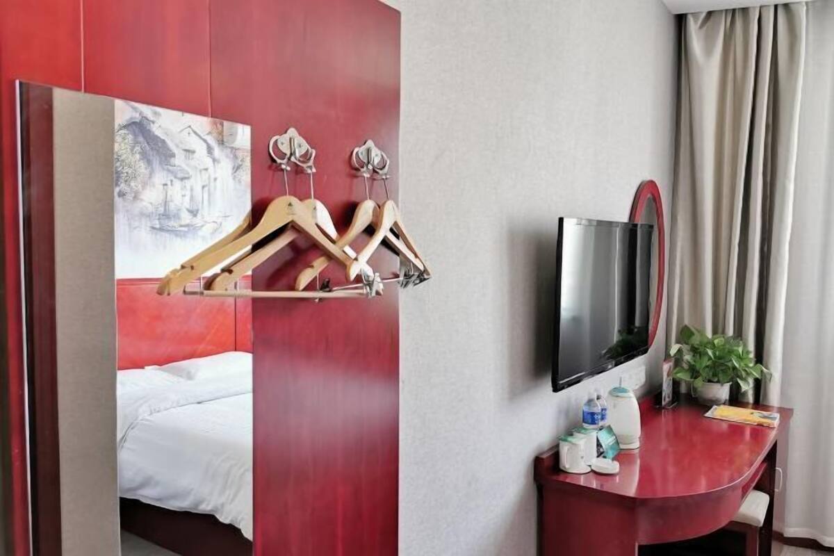A hotel room with a bed, a desk with a TV, a coat rack, and a painting on the wall.