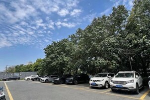 Un estacionamiento con varios coches aparcados bajo árboles.