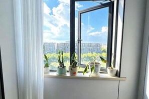 A window with a view of a cityscape, a curtain partially drawn, and several potted plants on a ledge. - Greentree Inn Jiangsu Suzhou International Film City South Jinshan Road Express Hotel (Suzhou)