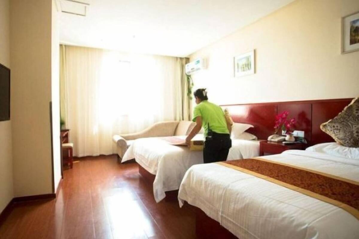 A hotel room with two beds, a wooden floor, a red headboard, and a window with curtains.