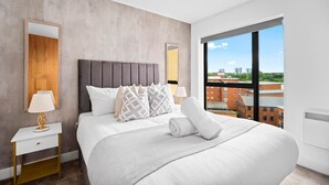 Ein modernes Hotelzimmer mit einem großen Bett, einem Nachttisch, einer Lampe und Blick auf die Stadt durch große Fenster.