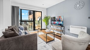 Ein modernes Wohnzimmer mit großem Fenster, Flachbildfernseher, weißem Heizkörper und grauer Wanduhr.
