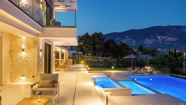 Ein moderner Poolbereich im Freien mit Bergblick, einer Lounge mit Sitzgelegenheiten und einem gut beleuchteten Weg.