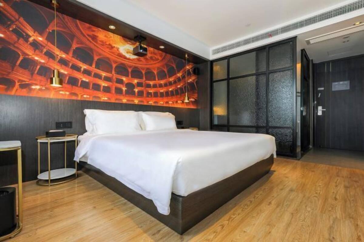 Une chambre d’hôtel moderne avec un grand lit, un parquet en bois foncé, une fresque murale et une grande fenêtre.