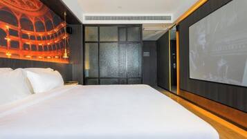 A hotel room with a large bed, a wall-mounted screen, and a theater-themed mural.