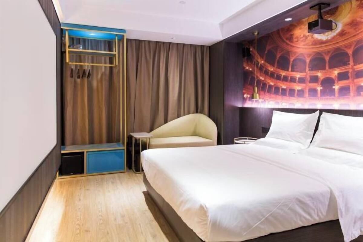 Une chambre d’hôtel avec un lit, une petite table, une chaise, un rideau et une fresque murale.